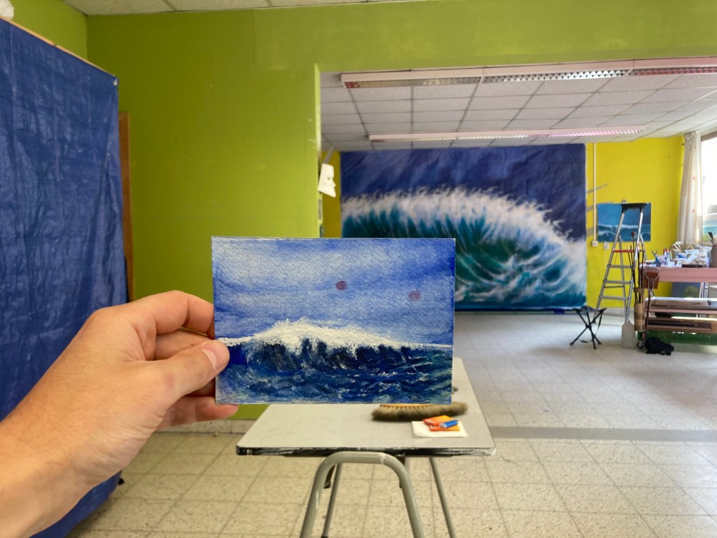 This miniature painting is currently on view at the East Frisia Biennial, which this year revolves around the theme Land am Meer. The piece, titled The Belgian Sea, was painted using tempera and oil paint on recycled cardboard.

There’s a beautiful story behind this work—or rather, it emerged through a gradual process. The starting point is the story of Petrus Dekker, a 76-year-old man, former paratrooper, and naval officer in the Dutch navy. He served as a commodore on large military vessels and sailed on nearly every type of warship. However, he had no background in painting.

Over time, through our conversations in the park and at the local café, Petrus shared his long-standing wish to create a monumental painting of the sea. After we visited the Anselm Kiefer exhibition together, with its monumental canvases and installations, I invited him to begin painting his sea in my studio, Studio Hipotetis.

There, he started painting seascapes on blue tarpaulins. Those works eventually inspired the creation of the miniature painting you see here.