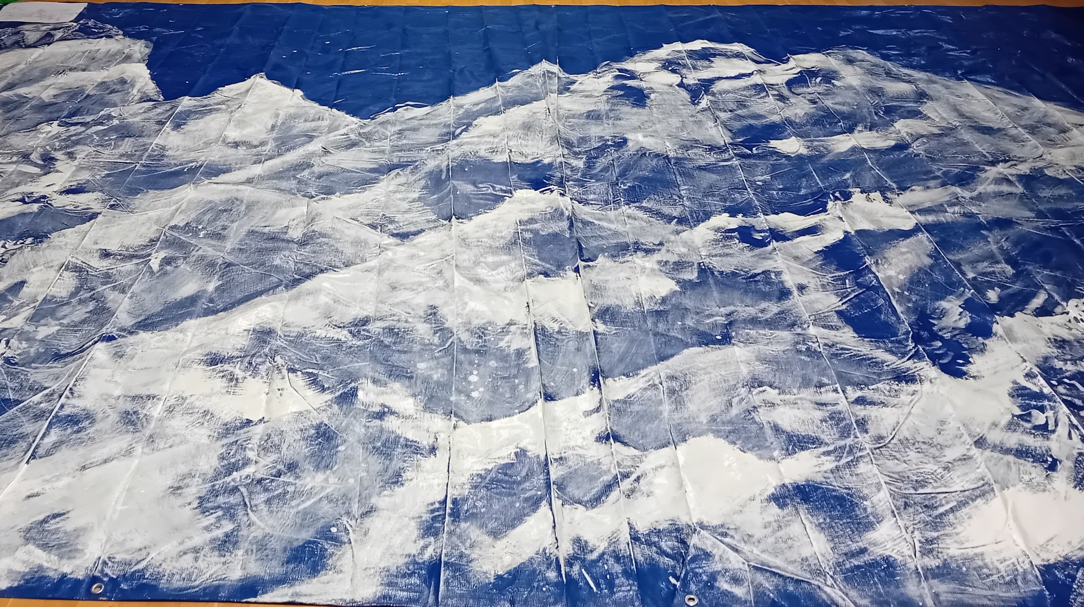 Large blue tarpaulin laid out in a room and painted together with alkyd enamel and oil paint during a short session on the word mountain